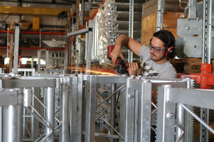 Een medewerker van Bouwma voert slijpwerkzaamheden uit aan metalen mastonderdelen van bouwmachines in de werkplaats.